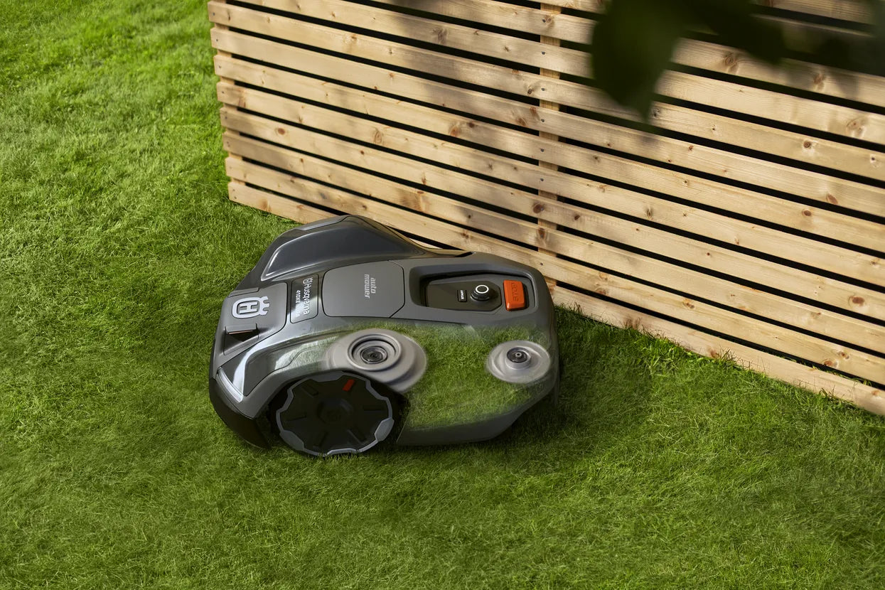 Robotic lawn mower 405XE on grass next to a wooden fence