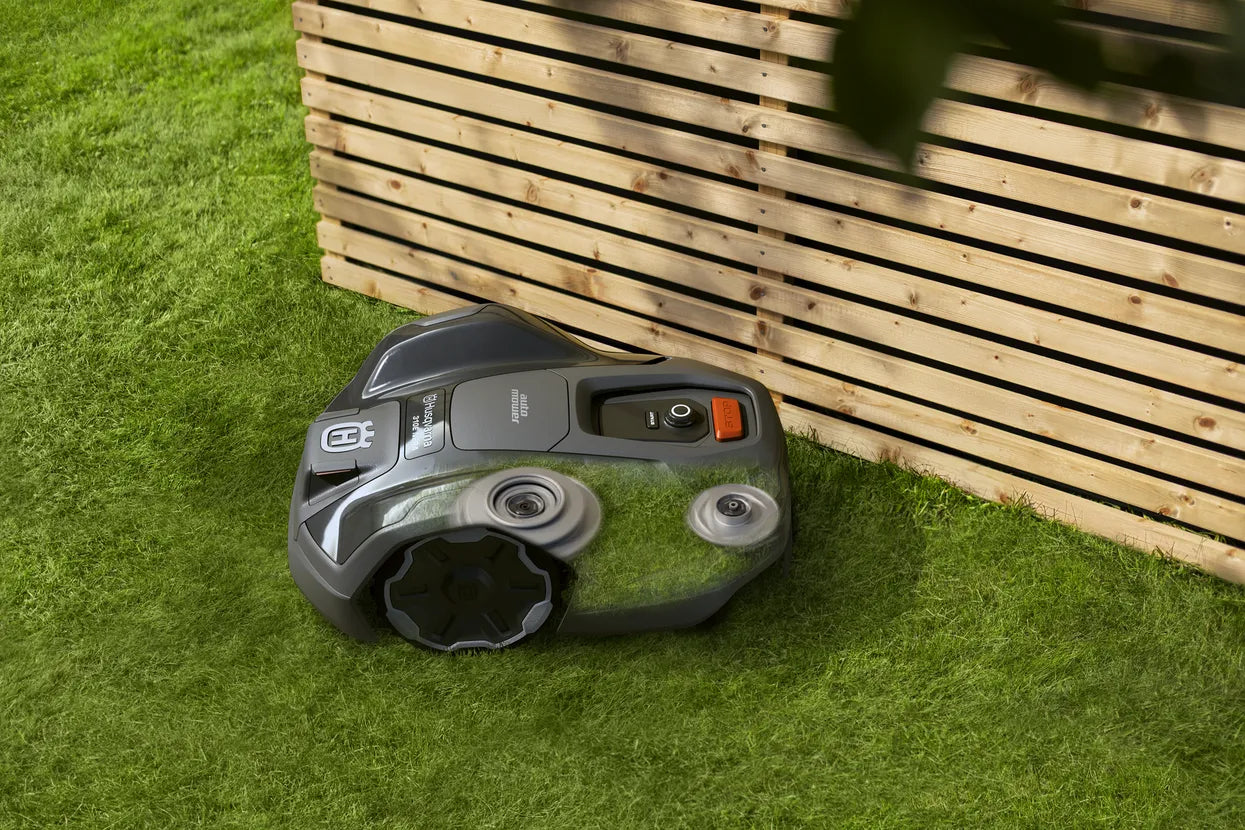 Husqvarna Automower 310E NERA Robotic lawn mower on grass next to a wooden fence with two cutting discs