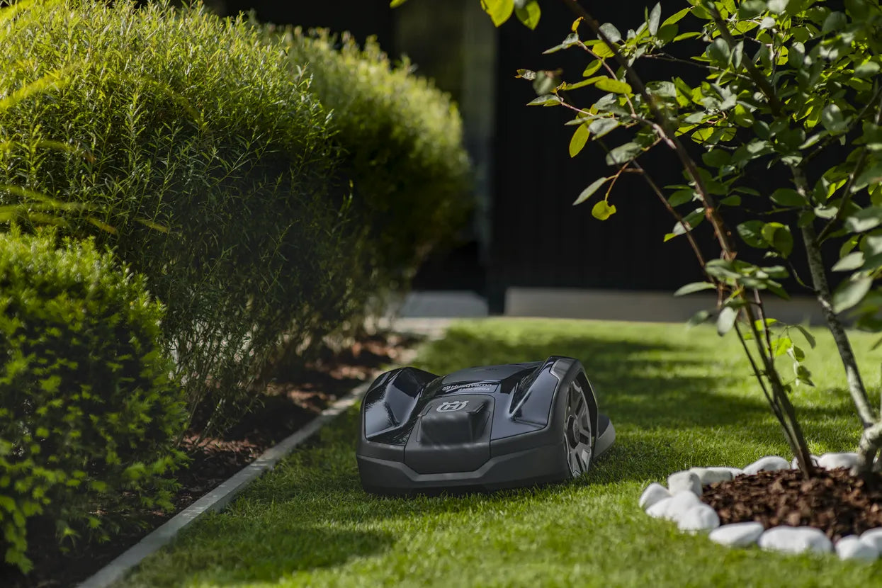 Husqvarna Automower 310E NERA Robotic lawn mower navigating through narrow passage on the lawn with bushes and plants around