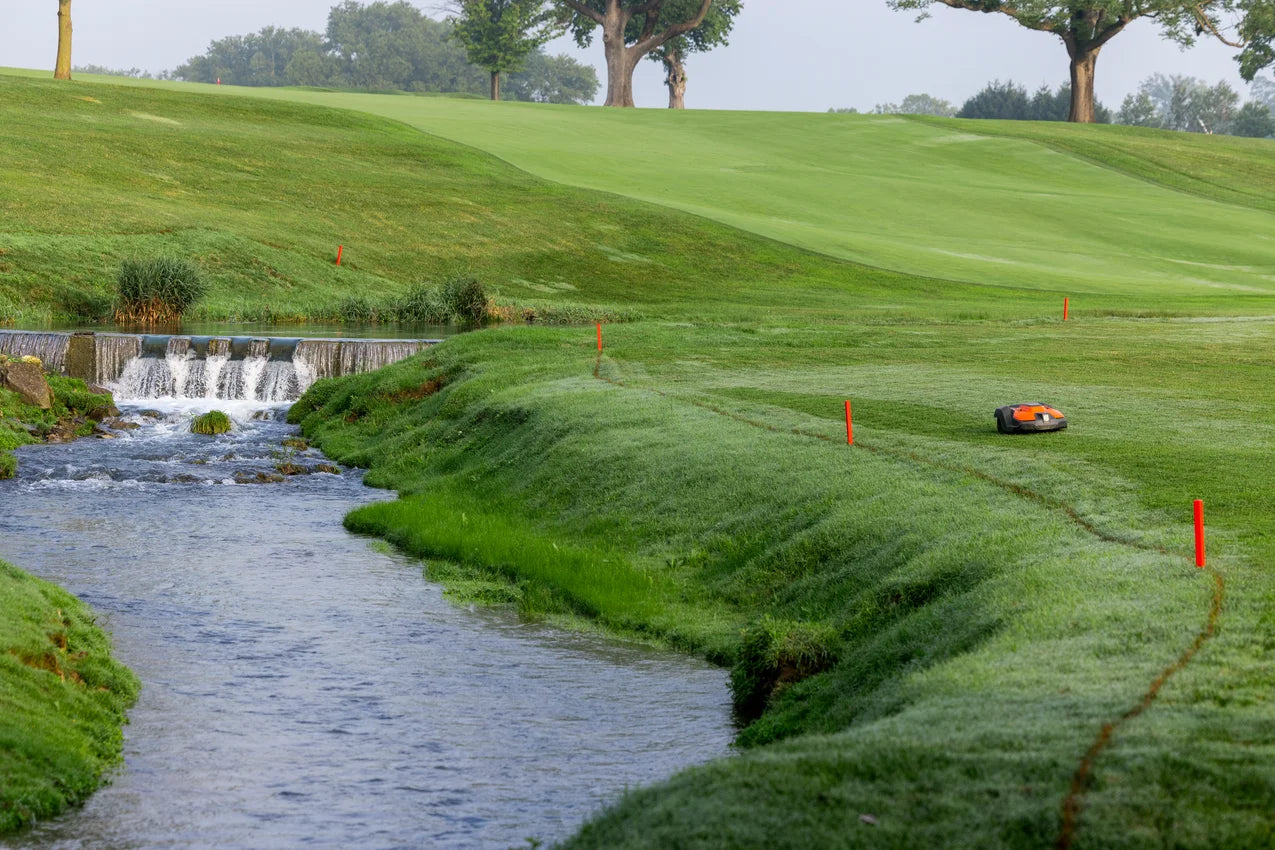Automower 550 EPOS on a Golf course with a stream, green grass, and trees in the background