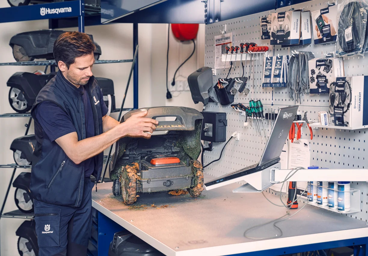 Person working on a Husqvarna lawn mower in a workshop setting.