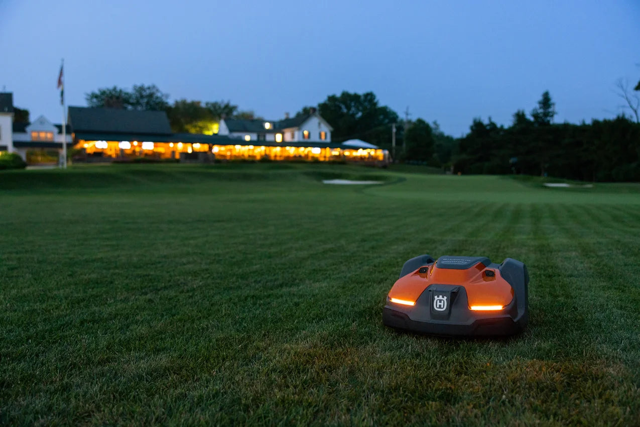 Automower 550 EPOS Commercial Robotic lawn mower on a grassy field at dusk with a house in the background