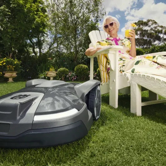 Woman relaxing on a lounge chair next to a Husqvarna Automower in a garden.