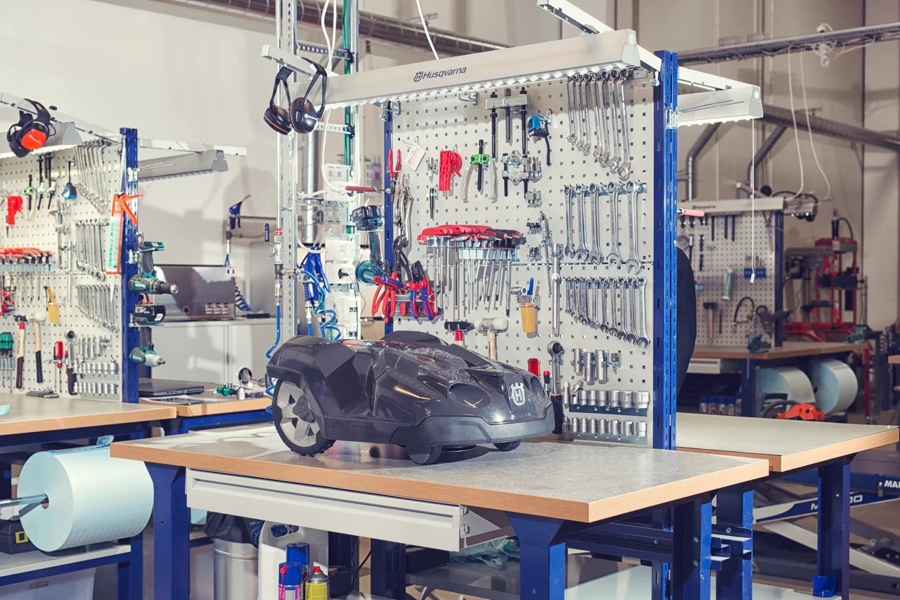 Husqvarna Automower in a workshop setting with tool storage system.