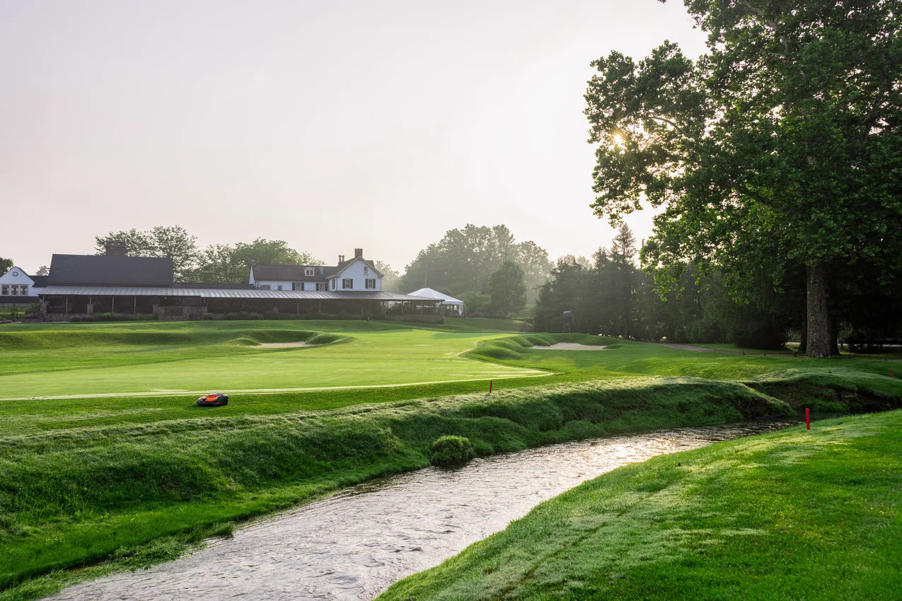 Golf course with green grass, trees, and a building in the background mowed by Automower 550 EPOS